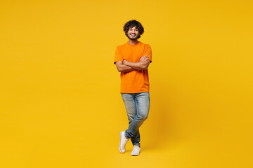 Full body young smiling happy cheerful Indian man he wears orange t-shirt casual clothes hold hands...
