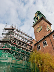 Fototapeta premium Historic Wawel Royal Castle restoration in progress, scaffolding partially covering medieval architecture, landmark clock tower rising against overcast skies in Krakow, Poland. Renovation of Wawel