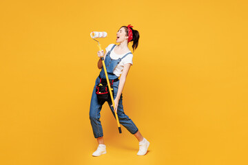 Full body young employee laborer handyman woman wear overalls belt hold use paint roller microphone...