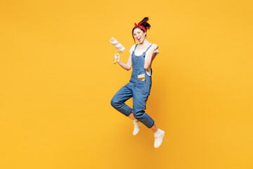 Fototapeta premium Full body winner young employee laborer handyman woman wear overalls belt hold paint roller isolated on plain yellow background. Instruments accessories renovation apartment room. Repair home concept.