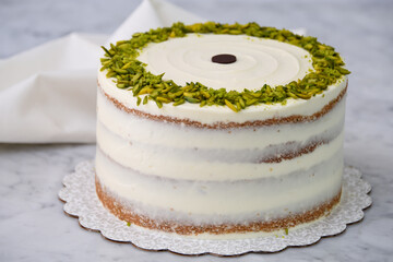 Elegant Pistachio Layer Cake featuring visible cake layers and a smooth white frosting decorated with chopped pistachios around with napkin on grey background closeup side view of delicious dessert