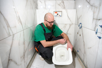 Plumber installing toilet. Modern bathroom installation. Worker installing a wall-hung toilet on...