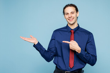 Young employee business man corporate lawyer wear classic formal shirt red tie work in office point index finger on empty palm with area isolated on plain pastel light blue background studio portrait.