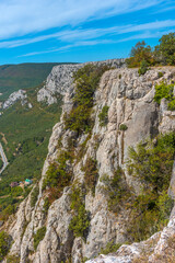 An impressive rocky cliff in the Crimean mountains overlooking a serpentine road that stretches along wooded slopes 