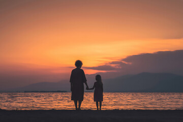 Fototapeta premium Silhouette of grandmother and granddaughter holding hands and enjoying a beautiful sunset over the sea
