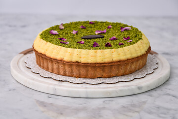 Pistachio Tart, featuring a creamy filling with pistachio topping, garnished with rose petals and a chocolate piece side view of baked dessert