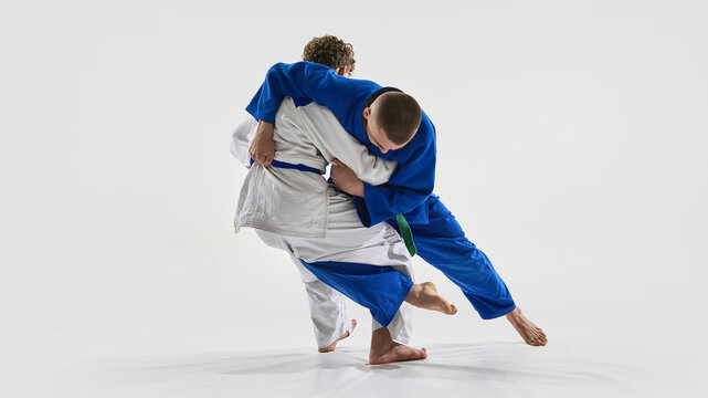 Fighters clash in low grapple stance, blue gi athlete preparing to unbalance opponent, capturing moment of strategy against white background. Concept of championship, victory, martial arts, action. - Powered by Adobe