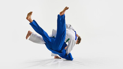 Powerful judo throw in motion as blue gi athlete flips mid-air, while opponent maintains grip,...