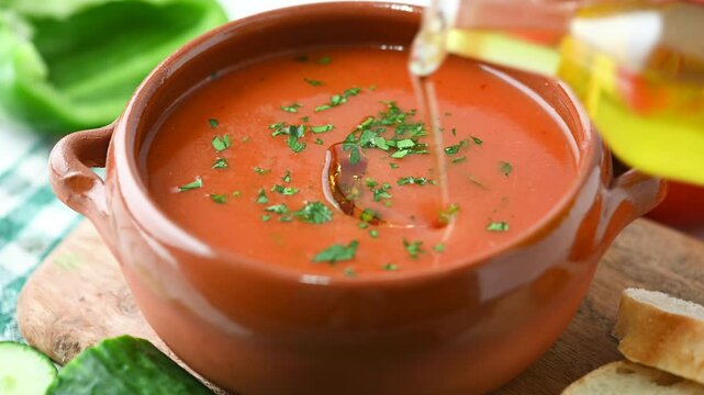 Pouring olive oil in traditional Spanish Gazpacho soup in bowl isolated on white background