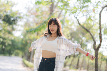 Asian woman enjoying summer outdoors, breathing fresh air with joyful expression, surrounded by...