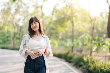 Asian woman enjoying summer outdoors, breathing fresh air in serene park with sunlight filtering...