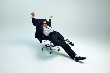 Young exhausted businessman reclining in rolling chair with loose posture and raised arm against...