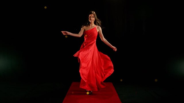 Stunning Black-Haired Woman in Ruby Red Dress and High Heels Gracefully Posing Against a Black Background, Captured in Super Slow Motion. Speed Ramp Effect.