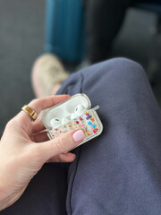 Female hand holding decorated earbuds case with airpods in casual setting - travel, lifestyle, accessories concept for tech brands
