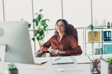 Confident businesswoman in casual attire working in a modern office setting surrounded by natural daylight and stylish workspace decor