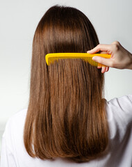 Woman with healthy brown hair with hair brush comb on white background, back view, isolation