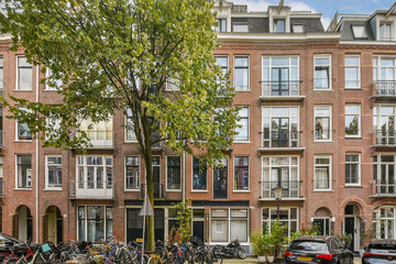Obraz premium A picturesque street in Amsterdam showcasing beautiful historic architecture, lush greenery, and parked bicycles that capture the charm of the city.