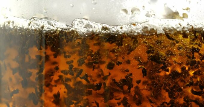The process of brewing black tea, boiling water is poured into a transparent cup with black tea leaves.