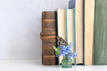 butterfly on blue flowers and books on table close up. Relax time, harmony of nature. Gentle...