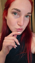 Close-up of a woman showcasing her newly tinted eyebrows. Her hand gently touches her chin while...