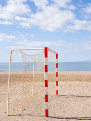Soccer goal standing on sandy beach under blue cloudy sky
