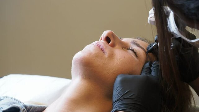 Esthetician applies microblading with blue tool on client eyebrow , slow motion frontal close-up