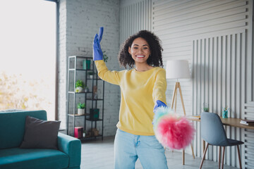 Smiling young woman cleaning at home with a duster, enjoying her time