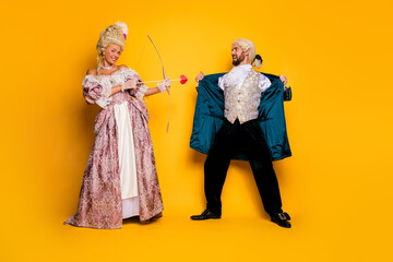 Playful couple in vintage costumes enjoying themed photoshoot on colorful yellow backdrop