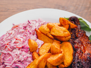 Simple meal with pork belly, potato wedges and pink coleslaw on white plate. Fine dinner with simple products.