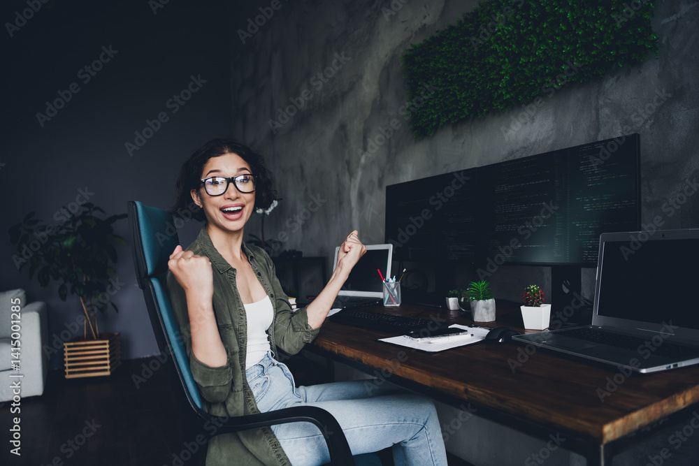 Poster excited female programmer celebrating success at her workspace with multiple monitors and a modern c