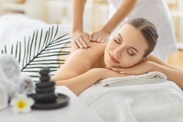 Young woman enjoying spa massage in salon, lying on table with closed eyes, enjoying relaxation...