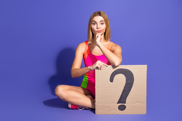 Charming Young Woman in Trendy Sportswear Holding a Cardboard Question Mark Against a Vibrant Purple Background