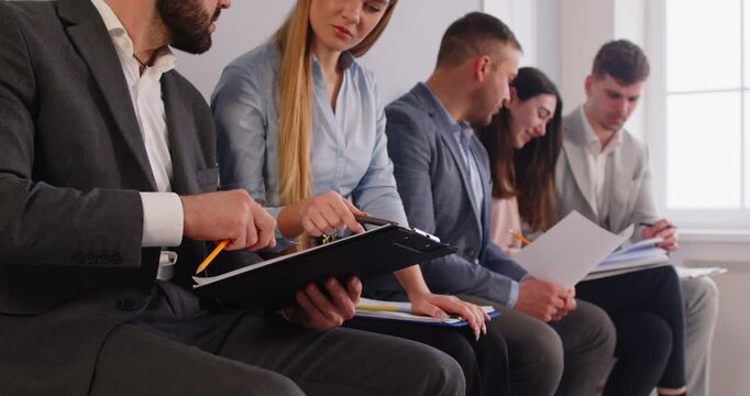 Cropped view of group of smiling job seekers sitting in line, preparing for interview in office. Male and female applicants discussing documents and resumes while waiting their turn. Human resources.