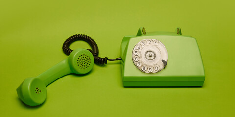 Classic green rotary phone in bold minimal composition on matching green background. Concept of retro aesthetics, vintage technology. Ideal for retro-themed banner, decor print, design, posters
