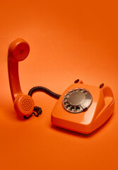 Orange vintage rotary dial telephone with receiver slightly lifted off its base is positioned...