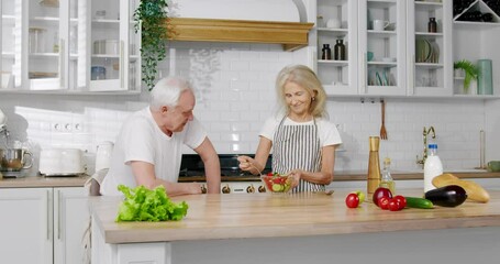 Happy family at kitchen, elderly woman cooking salad and husband refusing to eat . Healthy nutrition for lose weight and stay active in old age, vitamins in organic vegetables from eco farm for health