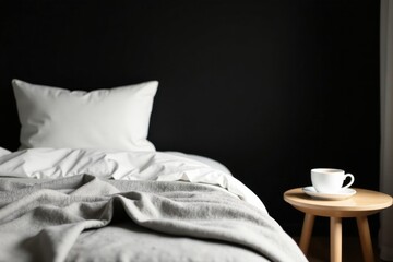 A cozy bedroom scene featuring a neatly made bed with a plush gray throw blanket, a white pillow, and a simple wooden side table holding a cup of coffee, perfect for a peaceful morning
