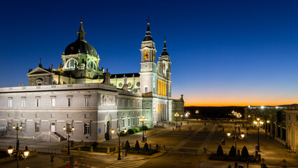 Fototapeta premium Almudena Cathedral (Santa Maria la Real de La Almudena) and Plaza de la Armeria night view after sunset, illuminated buildings, blue and orange sky, Madrid, Spain