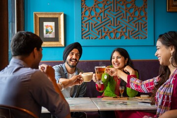 Group of South Asian friends enjoying drinks at a cafe. Smiling, chatting, and toasting. Happy...