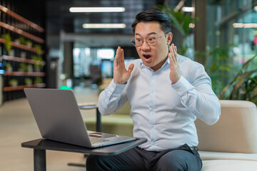 Chinese young businessman working on laptop shocked by sudden victory, game winning lottery goal...