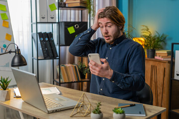 Caucasian young businessman using smartphone typing browsing, loses becoming surprised sudden...