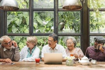 Group of diverse seniors enjoying conversation. Elderly friends, sharing laughter. Seniors, diverse, happy, together, chatting, smiling. Senior people using digital devices and social media.
