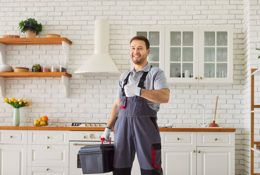 Happy plumber shows thumbs up after getting job done. Smiling confident reliable plumbing service specialist man with tool box standing in kitchen giving thumbs up after finishing sanitary repair work