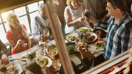 Group of women and men enjoying dinner at a restaurant. Diverse friends, wine, and laughter. Celebrating with food and drinks. Group of diverse friends enjoy dinning at restaurant with wine and food