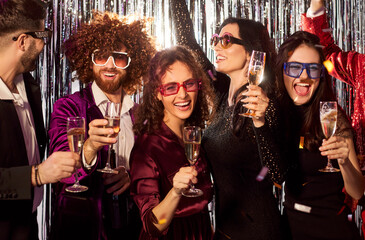 Group portrait of a happy and diverse friends dancing together while holding champagne glasses at a...