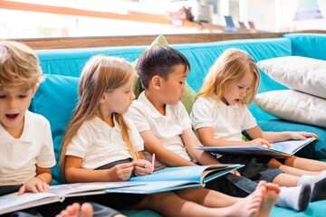 Children reading books on a couch. Kids in school uniforms, diverse group, focused on reading. Boys and girls enjoying books, learning together, reading time. Little kids reading books together.
