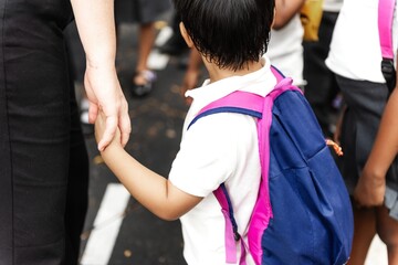 Child with backpack holding adult's hand. student and parent in outdoor setting. Student holding parent hand in front of school. Child wearing backpack, holding hand. Back to school.