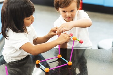 Two children building a 3D structure with colorful sticks and connectors. Diverse elementary students engaged in teamwork and creativity. Indoor educational activity for kids.