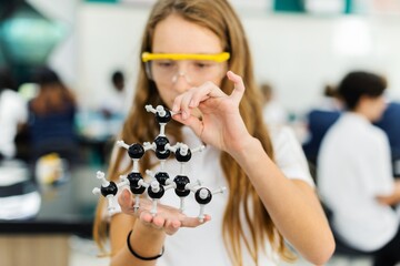 Young Caucasian girl in a science lab, holding a molecular model. The girl is focused on the...