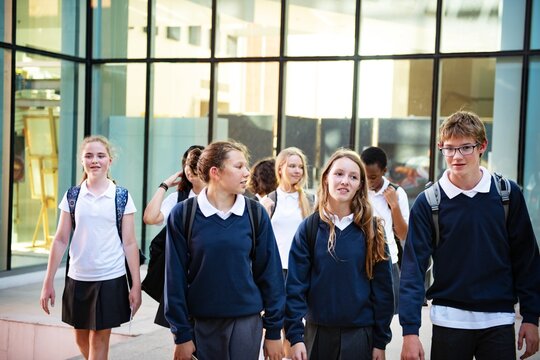 Group of teenage students, both boys and girls, wearing school uniforms. Students, mostly Caucasian, are walking and talking outside a school building. School uniforms and students.